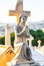 Angel statue with wings against tombstone cross in old cemetery. stone saint angel with praying hands at cemetery. Graveyard ancie