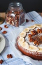 Angle view of cake with sliced banana, walnut and powdered sugar and glass jar full of nuts. Cozy still life in light tones on bac Royalty Free Stock Photo