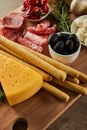 Angle view of cheese, breadsticks, salami slices, rosemary and bowls with antipasto ingredients on board on brown Royalty Free Stock Photo