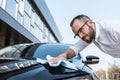 Angle view of happy businessman in glasses cleaning black car with white cloth near building