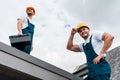 Angle view of happy handymen in helmets against sky with clouds