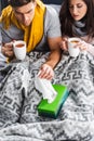 Angle view of sick girlfriend holding cup and boyfriend taking napkin Royalty Free Stock Photo