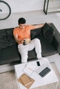 Angle view of young asian man sitting on sofa with bowl of popcorn and watching tv