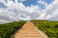 Angled closeup of stairs surrounded by greenery, blue sky with white clouds,