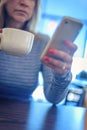 Angled closeup of woman checking smartphone and holding mug of c