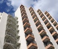 Angled detail view of an old 1960s white concrete apartment building with steps and balconies against blue sky and clouds