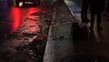 Angled shot of a wet sidewalk during the night where two persons` legs are visible Royalty Free Stock Photo