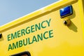 Angled view of EMERGENCY AMBULANCE sign on yellow NHS vehicle. Royalty Free Stock Photo