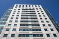 Angled view of a large, window covered apartment building corner against a blue, cloud filled sky Royalty Free Stock Photo