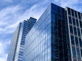 Angled view of a large, window covered building corner against a blue, cloud filled sky