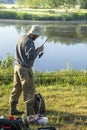 Angler in a hat and wellingtons is standing over the water with a fishing rod. Royalty Free Stock Photo