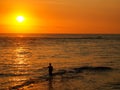 Angler silhouette holding fishing rod, fishing in shallow water of the ocean fishing at sunset