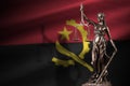 Angola flag with statue of lady justice and judicial scales in dark room. Concept of judgement and punishment