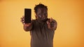 Angry african american black man showing phone screen and pointing finger towards camera. Cheated husband accusing his