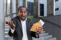 Angry african american businessman standing near office, bank. He holds an envelope with a letter Royalty Free Stock Photo