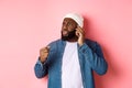 Angry african-american man talking on phone and threaten someone with raised fist, looking bothered at person, standing