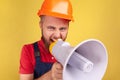 Angry aggressive bearded worker wearing protective helmet and blue overalls holding megaphone. Royalty Free Stock Photo