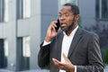 Angry and angry boss talking and shouting on mobile phone, african american businessman in business suit walking outside Royalty Free Stock Photo