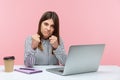 Angry annoyed woman in striped shirt sitting at laptop on workplace keeping fists clenched to punch, showing boxing gesture, ready Royalty Free Stock Photo