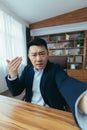 Angry Asian businessman boss talking on video call, using phone, working in classic office, arguing with employee, looking at Royalty Free Stock Photo