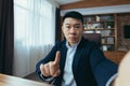 Angry Asian businessman boss talking on video call, using phone, working in classic office, arguing with employee, looking at Royalty Free Stock Photo