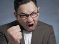 Angry Asian businessman showing his fist, ready to fight while screaming