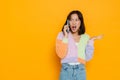 Angry asian girl talking on mobile phone and spreading hand over yellow wall Royalty Free Stock Photo