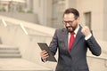 Angry bearded businessman dressed in blue suit threatening with fist to tablet during video conference outdoor office. Businessman