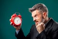 Angry bearded businessman holding alarm clock, shouting and showing fist at it. Time management concept Royalty Free Stock Photo