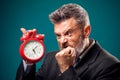 Angry bearded businessman holding alarm clock, shouting and showing fist at it. Time management concept Royalty Free Stock Photo