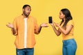Angry black woman showing smartphone with mockup to her boyfriend, blaming him for using online dating app