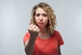 Angry blonde girl in casual t shirt raising hand furious at camera. Rage and aggressive concept