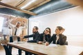 Angry boss with megaphone screaming at employees in office, scared and annoyed colleagues listening at the table