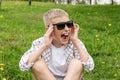 Angry boy in sunglasses sits on the grass and screams Royalty Free Stock Photo