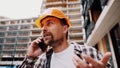 Angry builder, dissatisfied with deadline of work, swears at stress while talking to foreman on phone background of construction Royalty Free Stock Photo