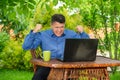 Angry businessman clenches fists and grits his teeth near laptop in backyard