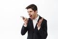 Angry businessman, entrepreneur scream at mobile phone, shouting in smartphone with furious tensed face, standing in