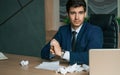 Angry businessman working with laptop in modern office. Crumples and throws sheets of paper.Problems in business of