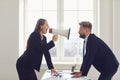 Angry businesswoman shouting into a megaphone at a worker man standing at a table in the office. Royalty Free Stock Photo