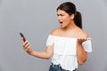 Angry casual woman using smartphone isolated on a gray background