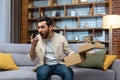 Angry cheated man at home with phone and boxed parcel received, arguing on phone talking to online store customer Royalty Free Stock Photo