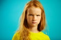 Angry children girl with red hair on blue.