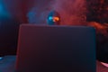 Angry computer hacker in suit stealing data from laptop illuminated by yellow and blue light