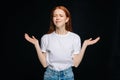 Angry confused young woman in T-shirt and denim with closed eyes spreads hands to sides