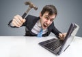 Angry and crazy man is working with laptop. He is going to damage notebook with hammer