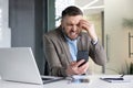 Angry and disappointed young male businessman sitting in the office at the desk and looking at the phone screen Royalty Free Stock Photo