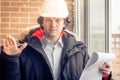 An angry disgruntled builder worker in a helmet with project drawings plans in his one hand and mobile phone in another Royalty Free Stock Photo