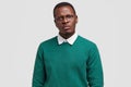 Angry dissatisfied black man frowns face has disappointed facial expression, vexed look, dressed in green jumper Royalty Free Stock Photo