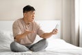 Angry mature asian man sitting on bed with phone Royalty Free Stock Photo