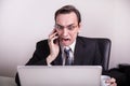 Angry and frustraded business man talking on a cell phone and screaming on his laptop in the office Royalty Free Stock Photo